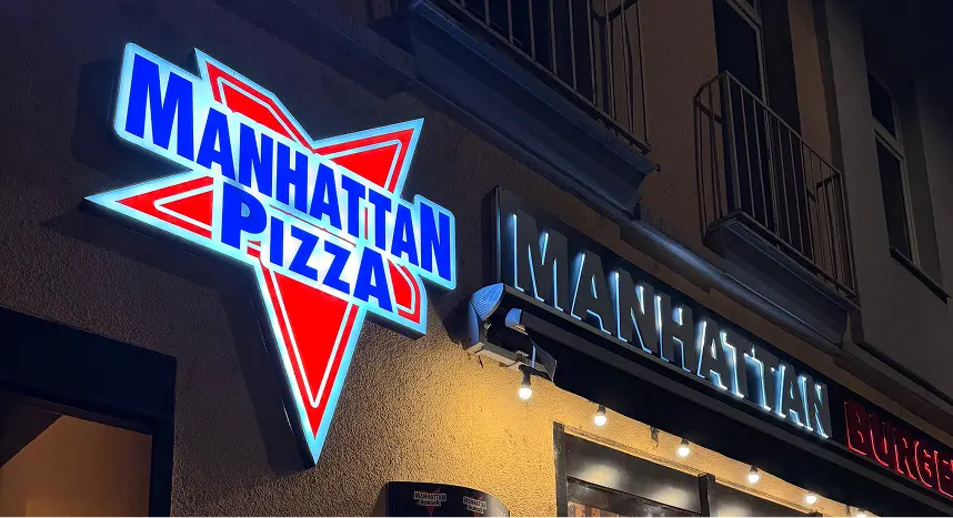 Außenansicht eines Manhattan Pizza Restaurants mit beleuchtetem Schild